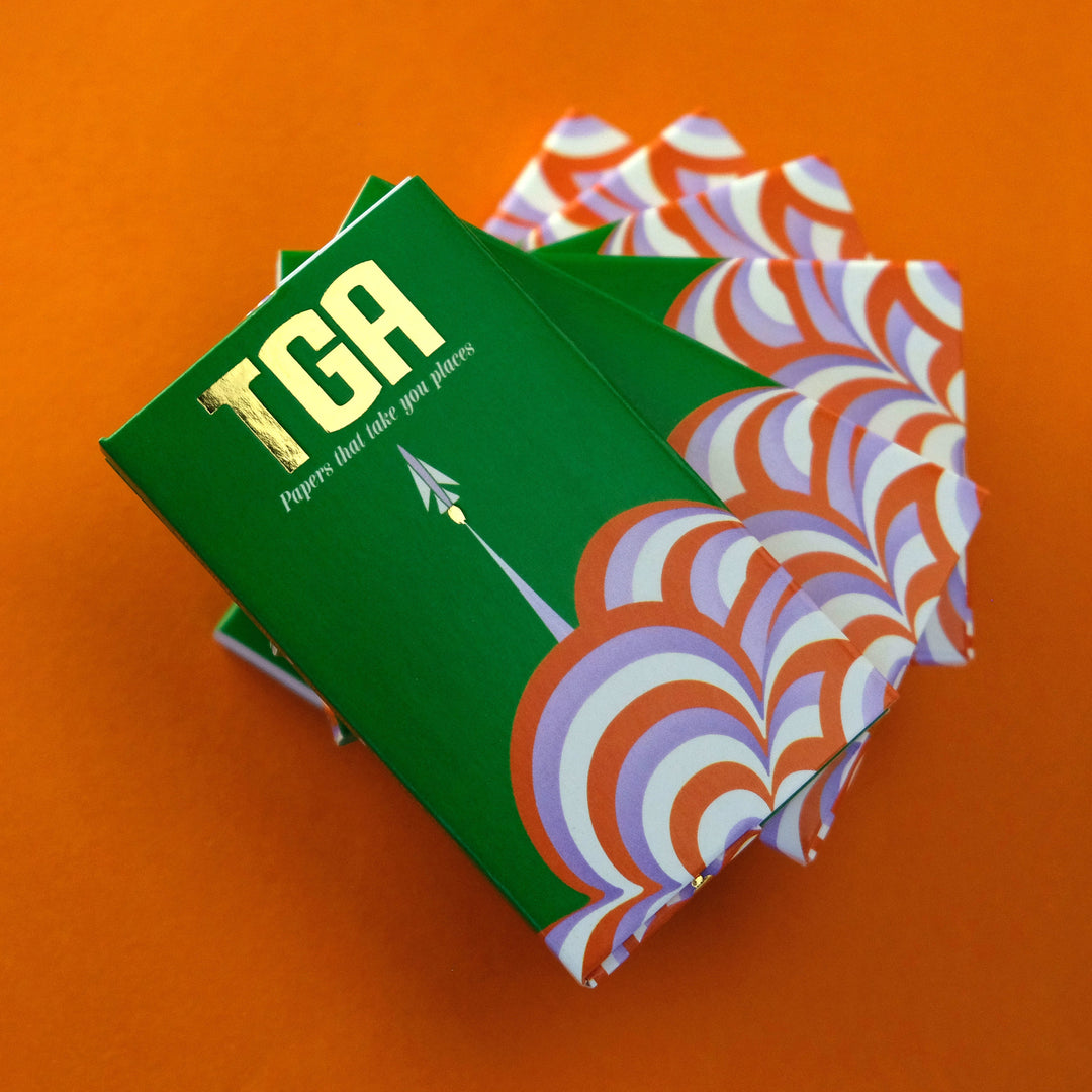 The Grass Agency Rolling Papers stacked and twirled on an orange background